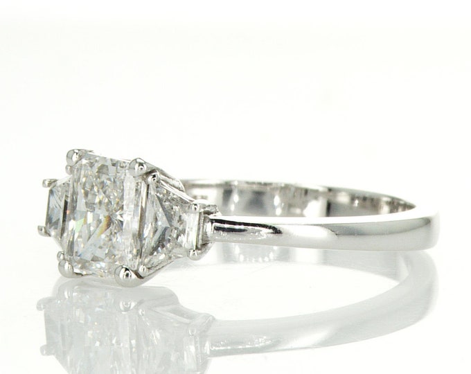 This Classic 14K Gold Three Stone Ring features a 2 Carat Radiant Cut accompanied by 2 Perfect Trapezoid Side Diamonds
