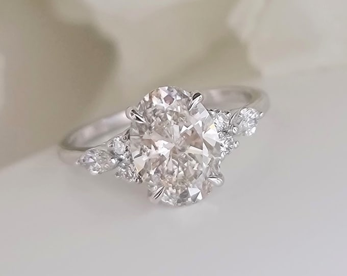 This vintage inspired engagement ring features a 2 carat oval IGI certified CVD lab grown center diamond accentuated with marquise and round cut diamonds