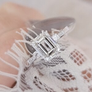 Può includere: Un anello di fidanzamento in argento con un grande diamante a taglio smeraldo e piccoli diamanti di accento sulla fascia.