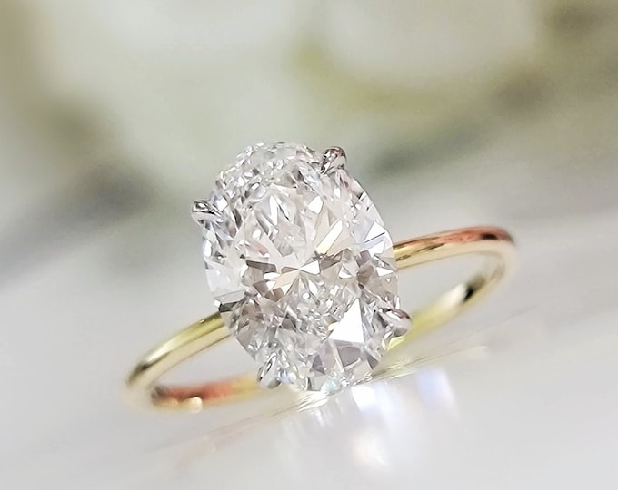 This unique oval engagement ring features a 2.50 Carat Oval cut IGI certified CVD lab grown diamond set in a 4 prong hidden halo 2 tone gold ring