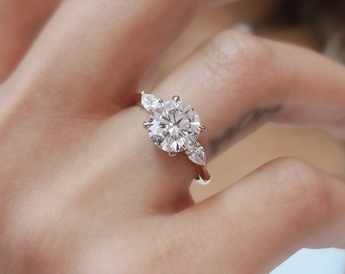 This Classic 14K Rose gold Three Stone Engagement Ring features a 2 carat Ideal round cut diamond and 0.20 carats teardrop side diamonds