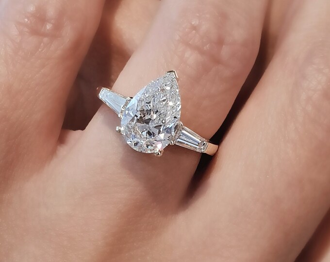This Unique Three Stone Ring features a 2.50 Carat Teardrop IGI Certified CVD lab grown diamond accentuated with 0.50ct tapered baguette side stones