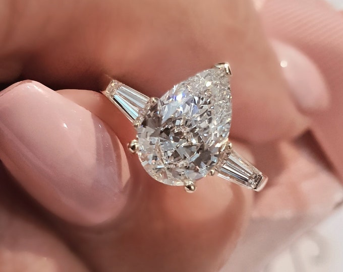 This Unique Three Stone Ring features a 3 Carat Teardrop IGI Certified CVD lab grown diamond accentuated with 0.50ct tapered baguette side stones