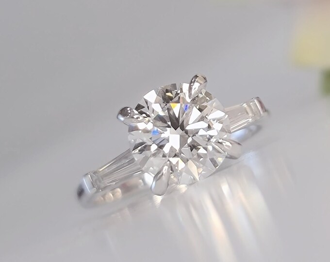 This classic timeless three Stone Diamond Ring features a 2.50 Carat Ideal Round Brilliant Cut IGI Certified CVD lab grown diamond accentuated with 0.50ct tapered baguette side stones