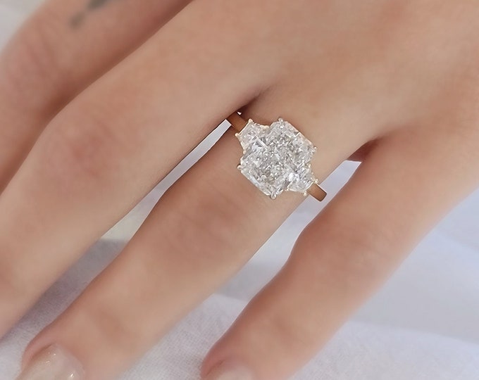 This Unique Two Tone Gold Three Stone Ring features a 3  Carat Radiant Cut IGI Certified CVD lab grown diamond accentuated with 0.50ct trapezoid cut side stones