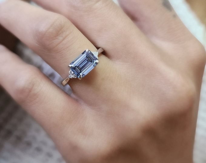 This unique EAST WEST setting features a 2.10 Carat Fancy Vivid Blue VS1 emerald cut CVD Lab Grown Diamond and 0.10 carats round brilliant cut side diamonds
