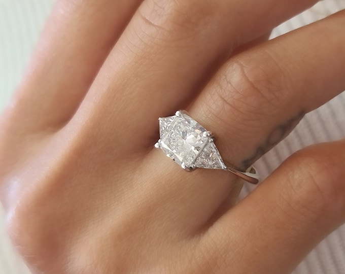 This Unique Three Stone Engagement Ring features a  2.5 Carat IGI Certified CVD lab grown Cushion Cut diamond accompanied by 0.70 carats triangle cut side diamonds
