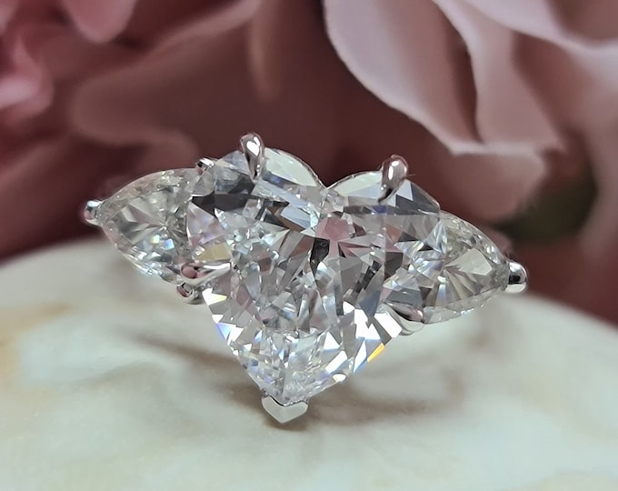 This Unique 14 Karat White Gold Three Stone Ring features a 3  Carat Heart Shaped IGI Certified CVD lab grown diamond accentuated with 0.70ct teardrop diamond side stones
