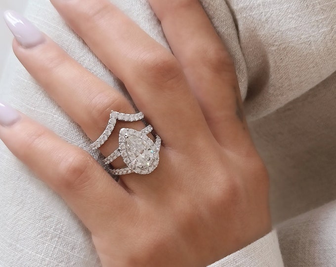 This unique ring set features  a split shank diamond pave setting with a 2.50 carat IGI certified CVD lab grown Pear cut diamond and 1.80 carat diamonds and is accompanied by a matching 0.70 carat diamond wedding  band