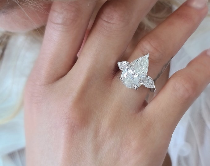 This Unique Three Stone Ring features a 6 Carat Teardrop IGI Certified CVD lab grown diamond accentuated with 1 carat pear cut side diamonds