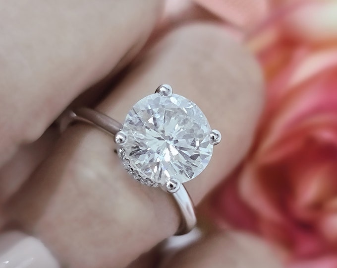 This dainty hidden halo solitaire setting features a 3 carat IGI certified CVD lab grown ideal round brilliant cut center diamond and 0.30 carats hidden accent diamonds