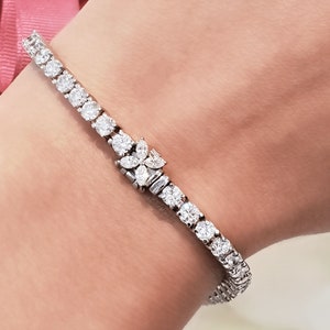 May include: A diamond tennis bracelet with a floral design clasp. The bracelet is made of white gold and features round and marquise-shaped diamonds.
