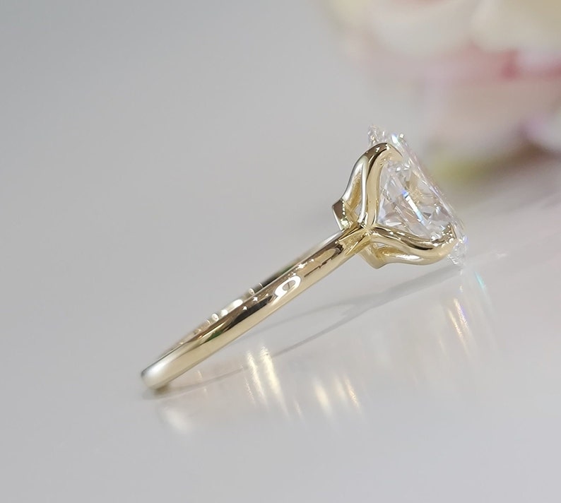 May include: A gold engagement ring with a large, clear oval-shaped diamond set in a prong setting. The band is thin and simple.