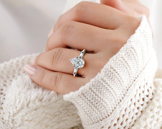 This Unique Three Stone Ring features a 2 Carat Teardrop IGI Certified CVD lab grown diamond accentuated with 0.50ct tapered side stones
