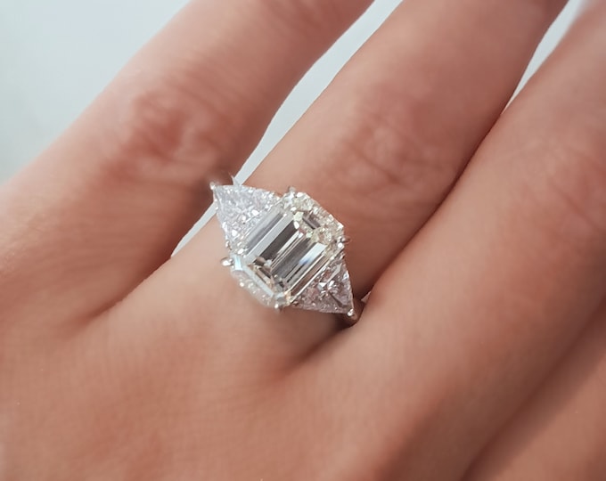This Unique White gold three Stone Ring features a 3 Carat Emerald Cut IGI Certified CVD lab grown diamond accentuated with 0.50ct Triangle diamond side stones
