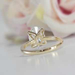 May include: A gold ring with a large oval-shaped diamond set in a flower-shaped setting. The ring is shown from the back, revealing the setting and the diamond's facets.