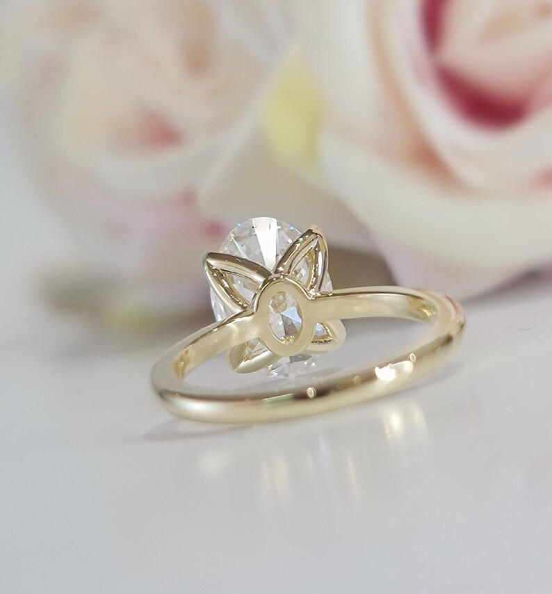May include: A gold ring with a large oval-shaped diamond set in a flower-shaped setting. The ring is shown from the back, revealing the setting and the diamond's facets.