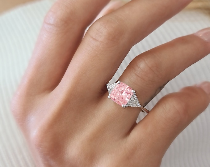 This Unique Three Stone Engagement Ring features a  3.5 Carat IGI Certified CVD lab grown Pink Cushion Cut diamond accompanied by 0.70 carats triangle cut side diamonds