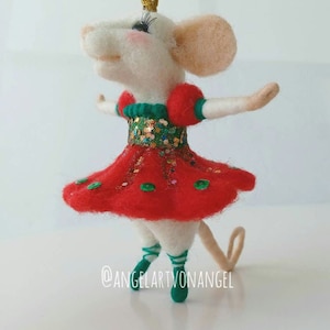 Pode incluir: Um rato de feltro branco vestindo um vestido vermelho e verde com glitter dourado e uma coroa dourada. O rato está usando sapatos de balé verdes e tem uma cauda longa.