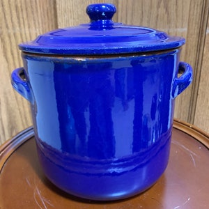 May include: A blue ceramic pot with a lid. The pot has two handles and a rounded shape.
