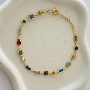 May include: A gold chain bracelet with colorful gemstones in various shapes, including squares, rectangles, and teardrops.