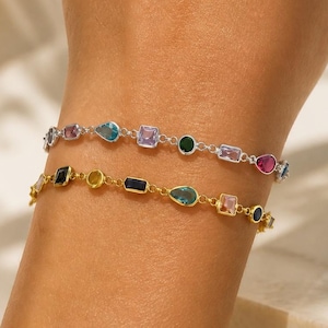 May include: Two delicate bracelets featuring a variety of multi-coloured gemstones in different shapes, including pear, square, and round cuts. One bracelet is set in a silver-toned metal chain, while the other is set in a gold-toned metal chain.