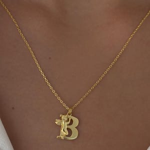 May include: A gold chain necklace with a pendant featuring the letter "B" with an angel figure on top.