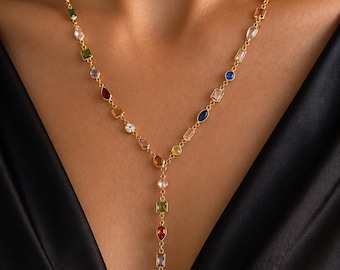 May include: A gold Y-shaped necklace featuring a delicate chain adorned with a variety of multi-colored gemstones in diverse shapes, including round, rectangular, and pear-cut stones in shades of blue, red, green, yellow, and clear white.