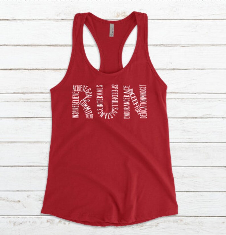 May include: Red racerback tank top with white text that reads "RUN" with words surrounding the letters, including "achieve", "inspire", "believe", "commit", "goals", "speed", "intervals", "strength", "endurance", "race", "effort", "dedication", and "mindset".