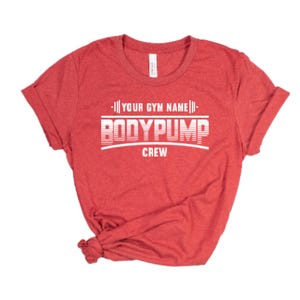 May include: Red t-shirt with white text that reads "[YOUR GYM NAME] BODYPUMP CREW".