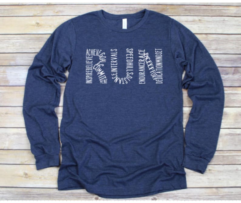 May include: A navy blue long-sleeve shirt with white text that reads "RUN" with words surrounding the letters, including "inspire", "believe", "commit", "achieve", "speed", "intervals", "strength", "endurance", "race", "dedication", and "mindset".