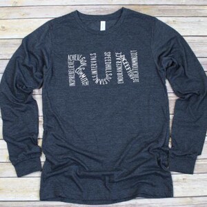 May include: A dark blue long-sleeved t-shirt with a white graphic design that spells out "RUN" using words related to running, such as "achieve", "inspire", "speed", and "dedication".