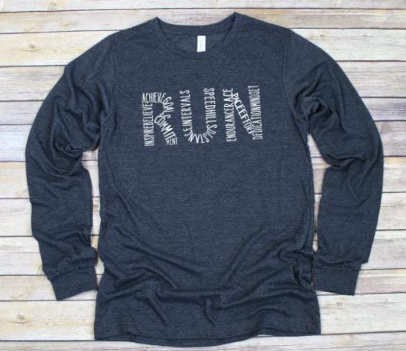 May include: A dark blue long-sleeved t-shirt with a white graphic design that spells out "RUN" using words related to running, such as "achieve", "inspire", "speed", and "dedication".