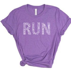 May include: Purple short-sleeved t-shirt with a white graphic design that spells out "RUN" using words related to running, such as "inspire", "believe", "goals", "speed", "hills", "intervals", "strength", "endurance", "grace", "effort", "dedication", and "mindset".