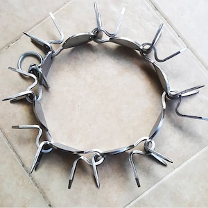 May include: A silver metal dog collar with sharp points. The collar is made of linked metal rings with a silver finish.