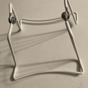 May include: White metal book stand with two adjustable arms. The stand is designed to hold books or other items upright.