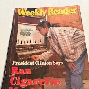 Puede incluir: Una portada de la revista Weekly Reader de noviembre de 1995 con el titular "President Clinton Says Ban Cigarette Machines". La imagen muestra a una persona mirando una máquina expendedora de cigarrillos. Revista vintage.