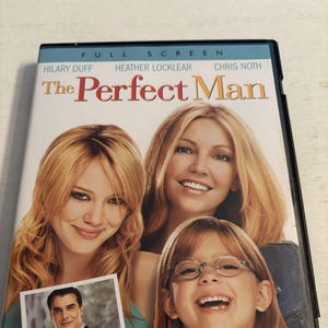 Puede incluir: Caja de DVD de la película "The Perfect Man" con Hilary Duff, Heather Locklear y Chris Noth. La portada incluye una foto de un hombre con traje y tres mujeres sonriendo. El título es rojo y blanco.