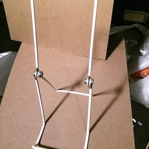 May include: White metal display stand with two adjustable legs. The stand is designed to hold a picture or other object upright.