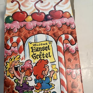 May include: Burger King Hansel & Gretel themed box. The box features a gingerbread house design with red cherries, pink frosting, and candy cane accents. The box has the words "WELCOME Hansel & Gretel" on a sign, with cartoon characters.