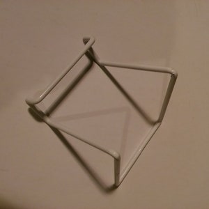 May include: White metal wire rack with a square shape. The rack is made of thin wire and has a simple design.