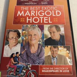 Op de afbeelding: DVD-hoes voor "The Best Exotic Marigold Hotel" met een rode, oranje en bruine gradiënt achtergrond. De cover bevat afbeeldingen van de cast, waaronder Judi Dench en Bill Nighy, en een motorfiets. Tekst bevat de filmtitel en de naam van de regisseur.