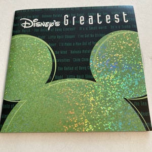 May include: A green CD with a holographic glitter finish featuring the Disney logo and the text "Disney's Greatest". The CD includes songs from popular Disney movies such as "The Ballad of Davy Crockett", "It's a Small World", "Hakuna Matata", and "Colors of the Wind".