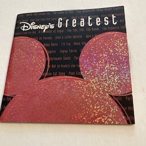 May include: A pink CD with a holographic finish featuring the text "Disney's Greatest" and a list of songs including "When She Loved Me", "He Lives in You", "The Wonderful Thing About Tiggers", "Can You Feel the Love Tonight", "What's This?", "Gaston", "Poor Unfortunate Souls", "A Spoonful of Sugar", "The Tiki, Tiki, Tiki Room", "The Siamese Cat Song", "Give a Little Whistle", "Who's on Parade", "Alma Mater", "I'll Try", "When She Loved Me", "Topsy Turvy", "Unfortunate Souls", "Part of Your World", "Yo Ho! (A Pirate's Life For Me)", "Pink Elephants on Parade", and "The Siamese Cat Song".