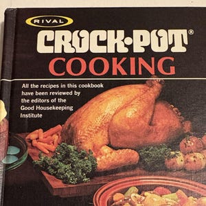 May include: A hardcover cookbook titled Rival Crock-Pot Cooking with a black cover featuring a roasted chicken, carrots, and potatoes. The text states that all recipes have been reviewed by the editors of the Good Housekeeping Institute.