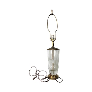 May include: A brass table lamp with a clear glass shade featuring a cut-glass design. The lamp has a cord and a standard light bulb.