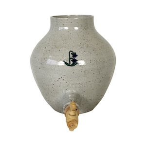 May include: A white ceramic pitcher with a speckled glaze and a floral design. The pitcher has a wooden spigot.