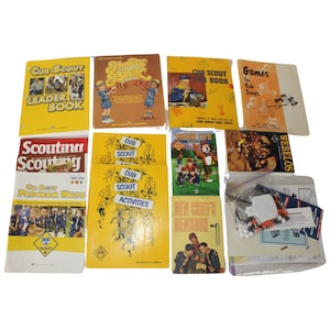 May include: A collection of vintage and modern Boy Scout books and manuals. The books are yellow, blue, and red with titles like "Cub Scout Leader Book", "How to Book", "Cub Scout Fun Book", "Games for Cub Scouts", "Scouting Scouting", "Cub Scout Activities", "Tiger Cub", "Den Chiefs Denbook", and "Webelos".