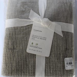 May include: A gray linen waffle weave sham, packaged in a clear plastic bag with a white ribbon. The sham is labeled "Standard Belgian Flax Linen Waffle Weave Sham" and "Responsibly Made" with the dimensions 26 x 20 inches (66 x 51 cm).