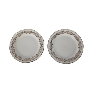 Puede incluir: Dos platos de cerámica blanca con un diseño floral dorado alrededor del borde.